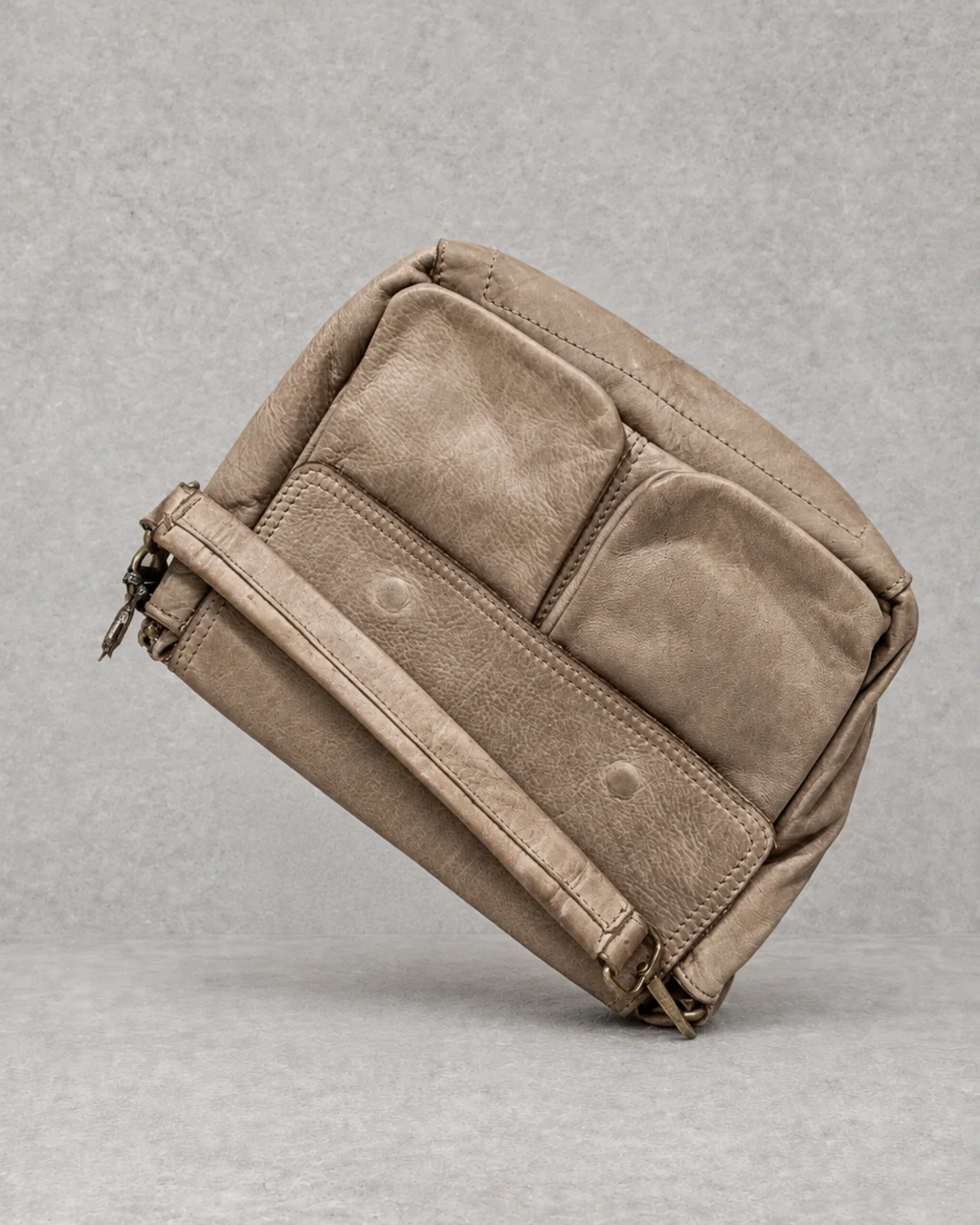 Bolso taupe de piel sobre fondo cemento gris, vista exterior