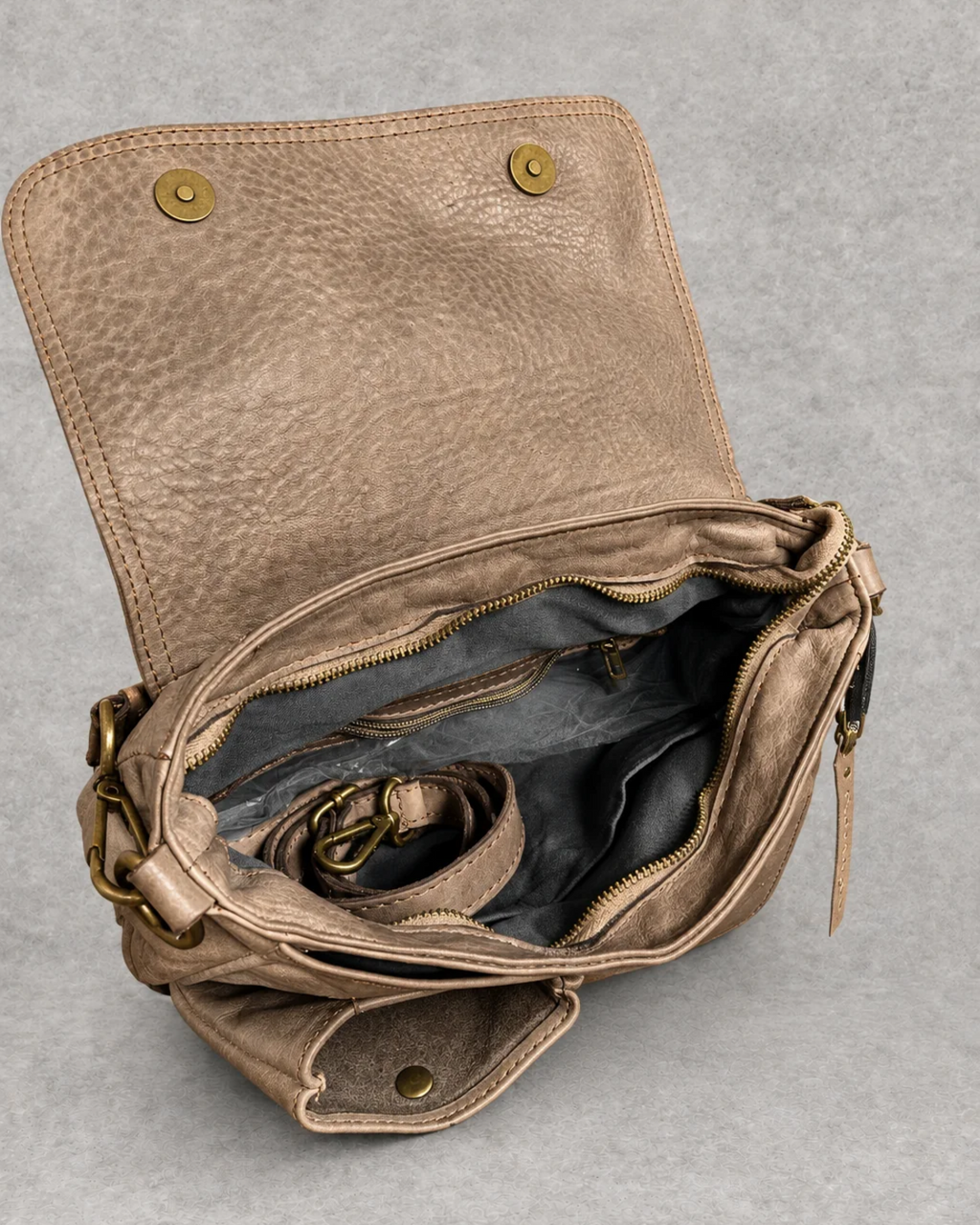 Bolso taupe de piel abierto sobre fondo cemento gris, vista interior