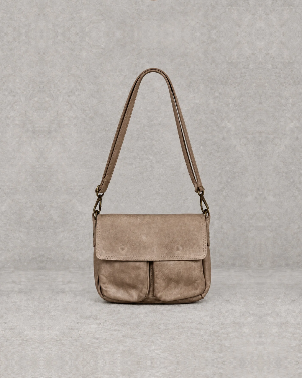 Bolso taupe de piel sobre fondo cemento gris, vista frontal