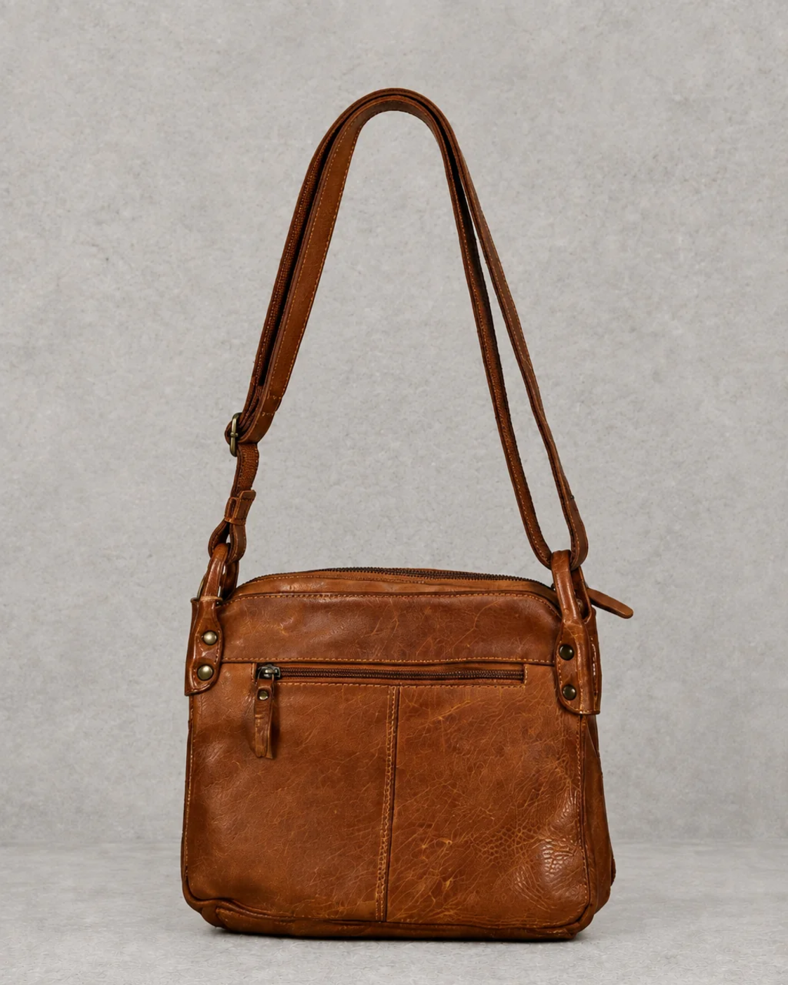 Bolso marrón de piel sobre fondo cemento gris, vista trasera